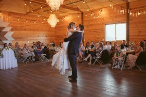 Wedding reception dance party in a warmly lit rustic barn venue.