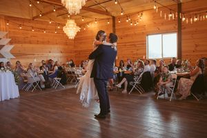 Wedding dance in a rustic wood-paneled venue with guests seated at reception tables.