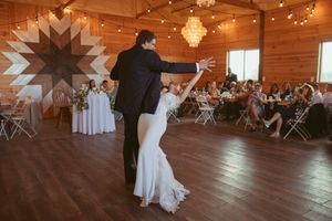 A couple dances in a rustic wooden venue decorated with string lights and chandeliers during a wedding celebration.
