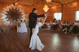 A couple shares their first dance in a rustic wooden reception hall adorned with chandeliers and string lights.