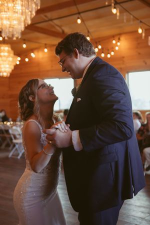 Couple shares a romantic dance under glowing string lights and chandeliers at a wedding reception.