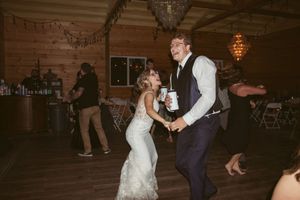 Wedding guests dance together on rustic wooden dance floor under warm lighting.