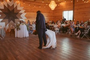 Wedding party dances under warm lighting and string lights in a rustic wooden barn reception venue.