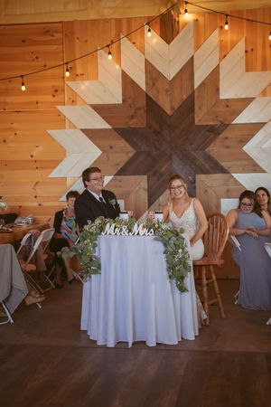 Wedding reception venue decorated with geometric wood wall art, string lights and round tables with white linens.