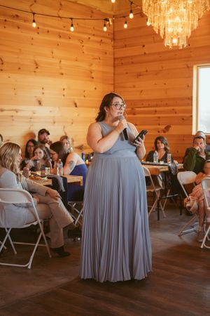 Wedding reception in a wooden barn interior with crystal chandeliers and guests seated at folding tables.