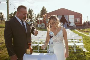 Couple sharing a joyful moment during outdoor sunset ceremony with white chairs and red barn in background.