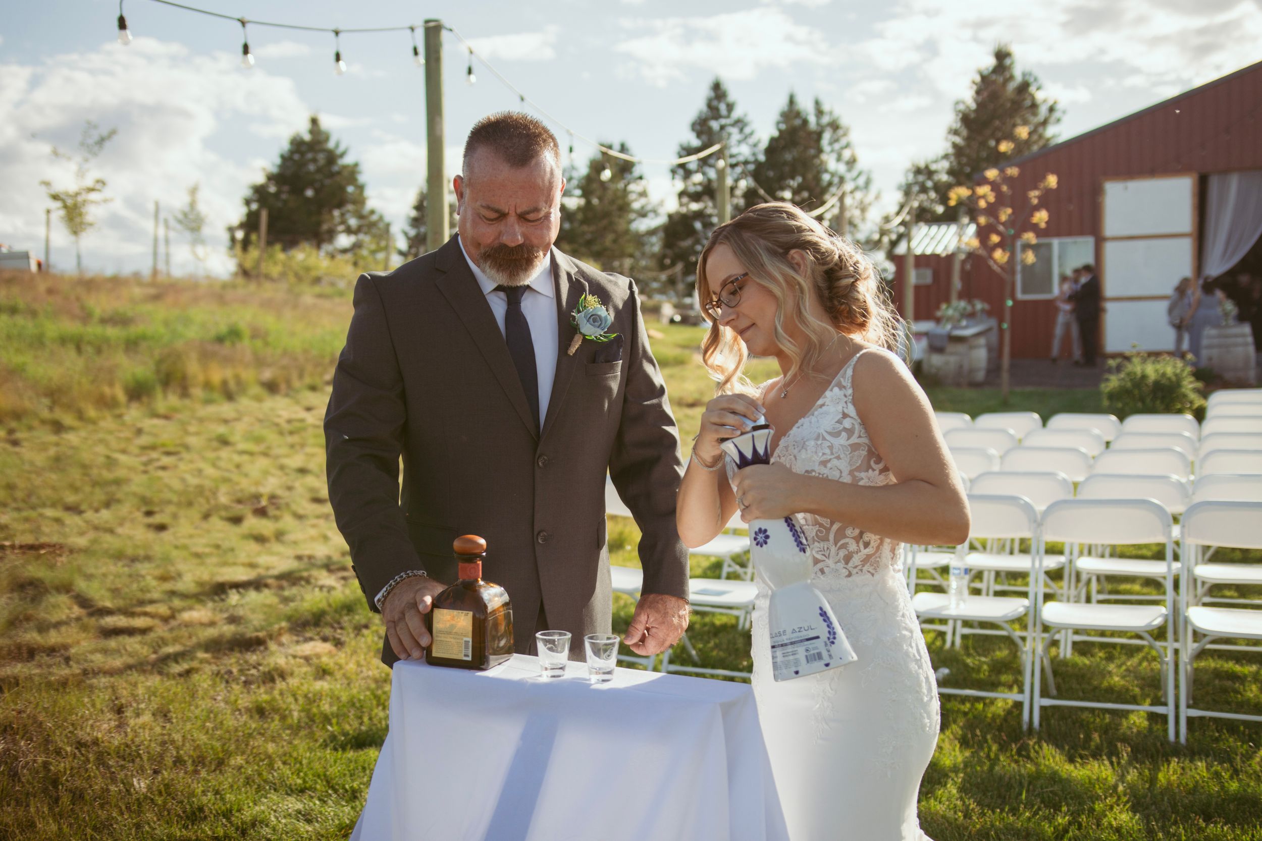 Wedding celebration outside with string lights and white chairs set up on a lawn at sunset.