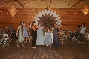 Couples dancing at a rustic barn wedding reception under string lights and crystal chandeliers.
