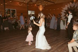 A bride in a white lace dress dances with party guests on a wooden dance floor decorated with string lights.
