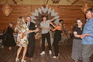 Guests dancing and celebrating on wooden dance floor at a rustic barn reception with string lights overhead.