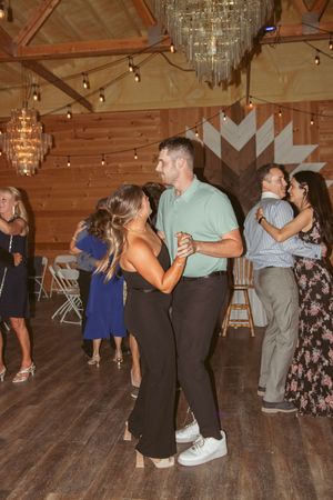 Wedding guests dancing on hardwood floor beneath crystal chandeliers and string lights.