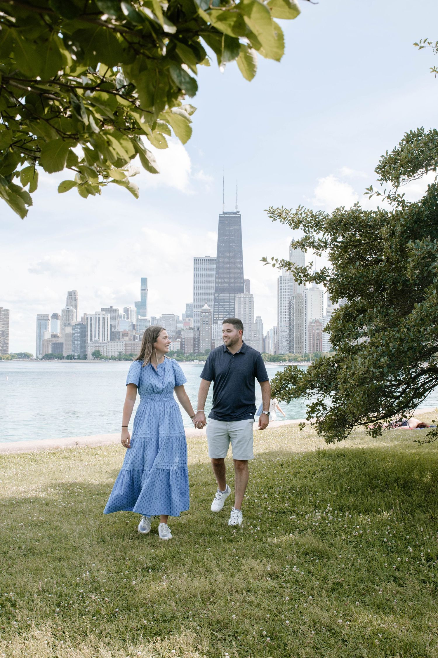 Couple strolls along Lake Michigan shoreline with Chicago skyline in background during summer afternoon.