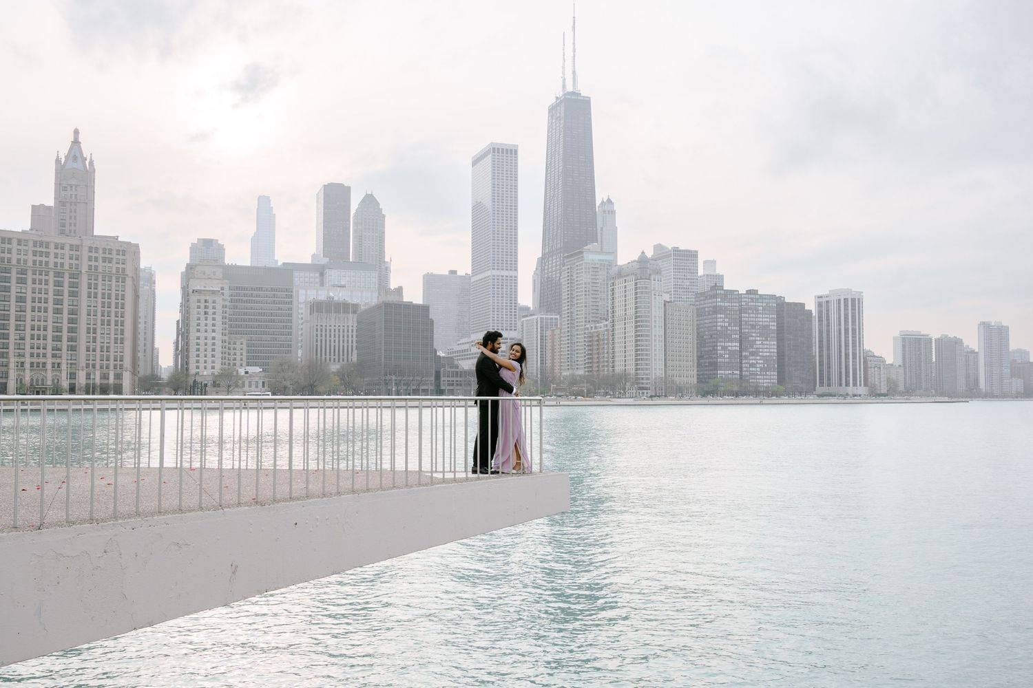 A couple embraces on a foggy morning along Lake Michigan with Chicago's iconic skyline in the background.