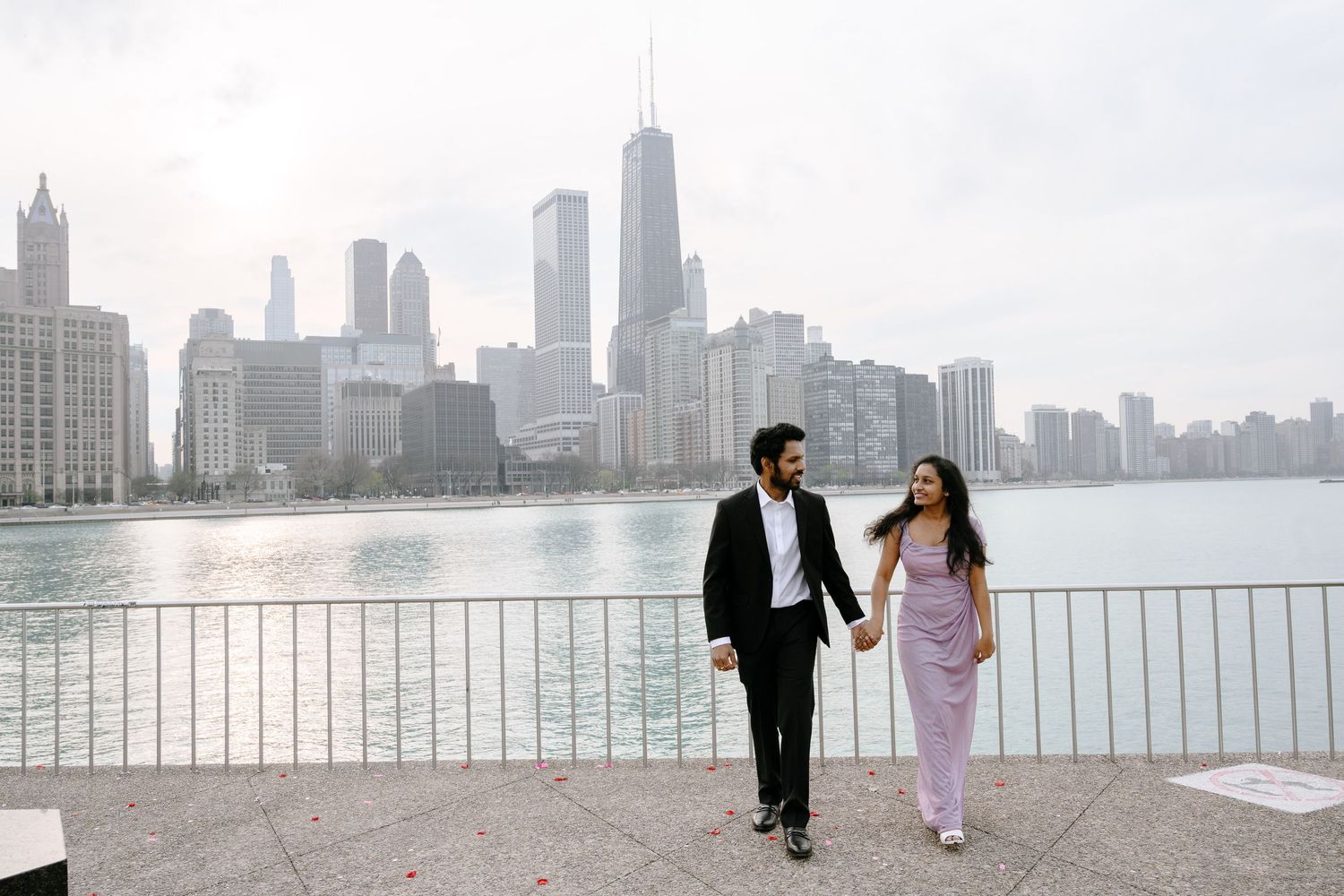 A couple walks along Lake Michigan with the iconic Chicago skyline in the background on a misty morning.
