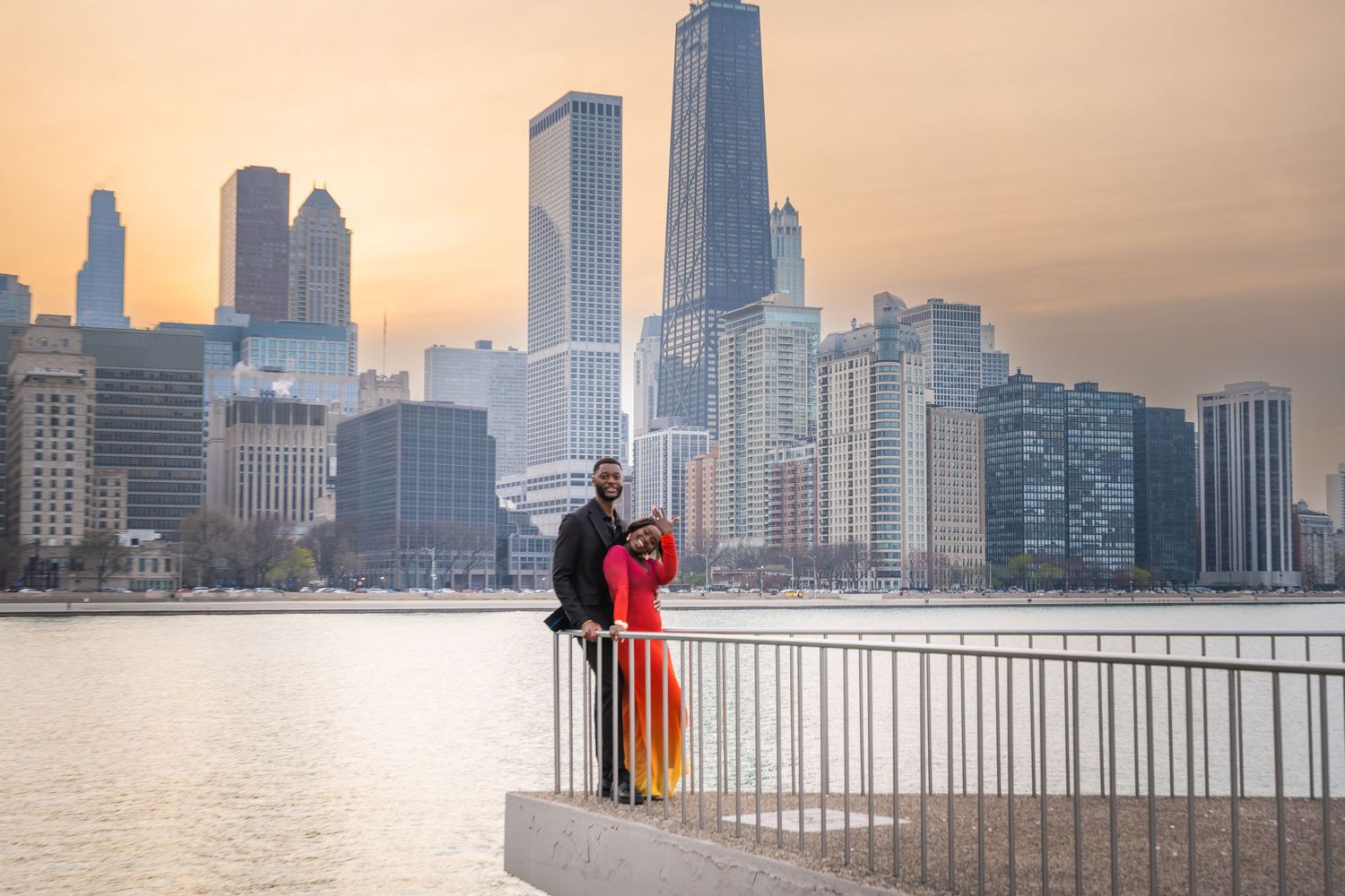 People enjoy views of Chicago's skyline along Lake Michigan at sunset as skyscrapers cast reflections on calm waters.