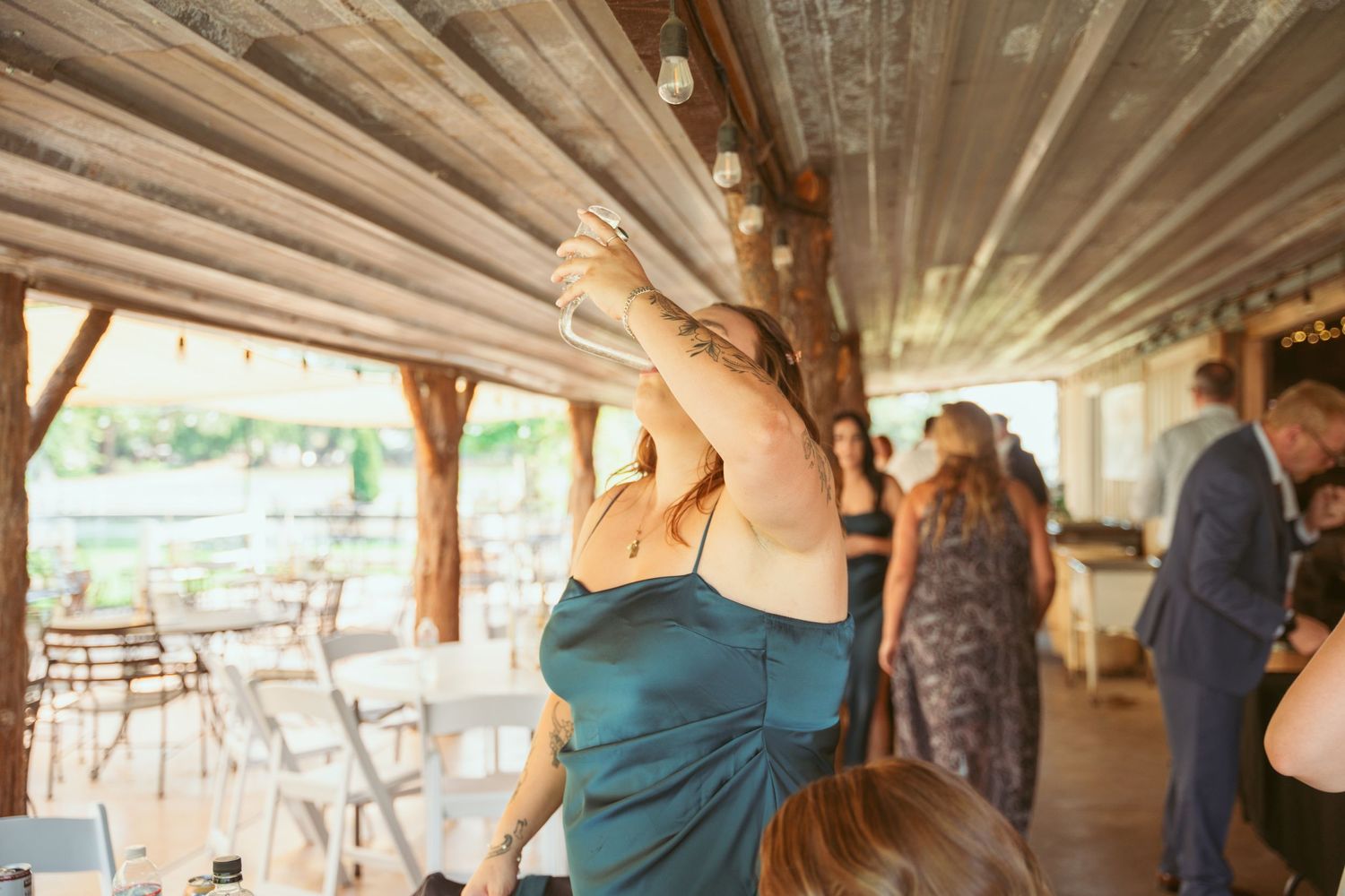 Guests dance and celebrate at a rustic outdoor venue with draped fabric ceiling and natural lighting.