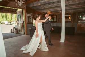 A couple dances their first dance at a rustic barn wedding venue with white drapery and romantic lighting.