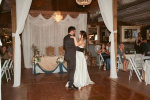 A wedding couple dances during their first dance in a rustic wooden barn venue with romantic lighting.
