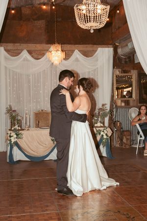 A romantic first dance at a wedding reception beneath crystal chandeliers with elegant drapery and decor.