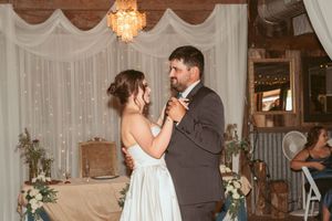 A romantic dance moment at a rustic wedding venue with sparkling chandeliers and white draping in the background.
