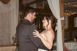 Couples slow dancing under romantic string lights at an indoor wedding reception with white fabric decor.