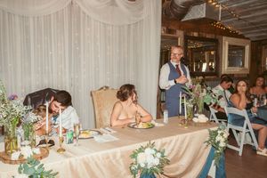 Wedding reception head table decorated with white linens and floral centerpieces.