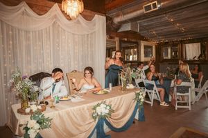 Wedding reception in a rustic venue with elegant decor featuring a head table with navy and ivory details and floral arrangements.