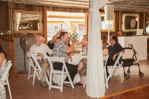 Wedding reception guests seated at tables inside a rustic-style venue with wooden beams and string lights overhead.