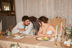 A couple enjoys their wedding dinner at an elegantly decorated sweetheart table with candles and floral arrangements.