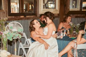 Wedding guests celebrate with laughter and hugs at a rustic reception with string lights and industrial decor.
