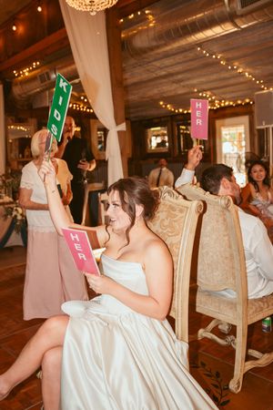 Wedding guests playing a game with colored cards in a rustic barn venue decorated with string lights.