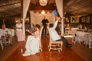 Wedding party members participate in a fun shoe game on a wooden dance floor under string lights.