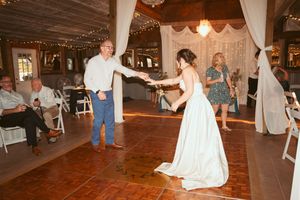 A couple dances on a wooden floor during their wedding reception in a rustic barn venue.