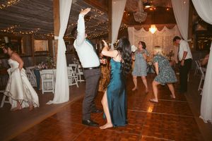 Wedding reception dance floor filled with guests under string lights and white fabric decor.