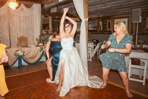 Guests dancing joyfully at a rustic reception venue decorated with string lights and white fabric draping.