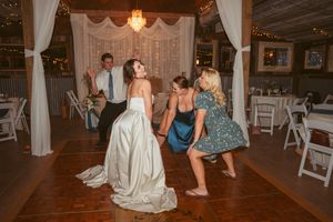 Lively dancing scene at a rustic barn wedding reception with white drapes and string lights overhead.