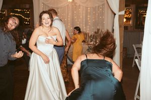 Wedding guests dancing and celebrating on the dance floor with white curtains and lighting in background.