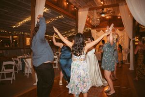 People dancing and celebrating at a wedding reception in a rustic barn with twinkling lights overhead.
