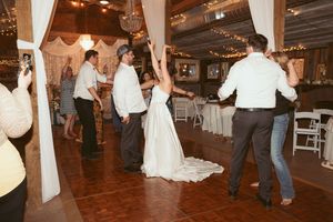 People celebrate on the dance floor at a wedding reception with white draped columns and twinkling lights.