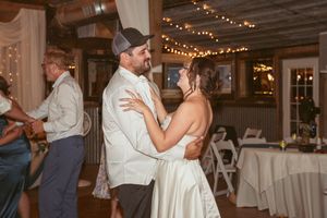 Guests dancing and celebrating at a wedding reception with string lights and white drapes decorating the rustic venue.