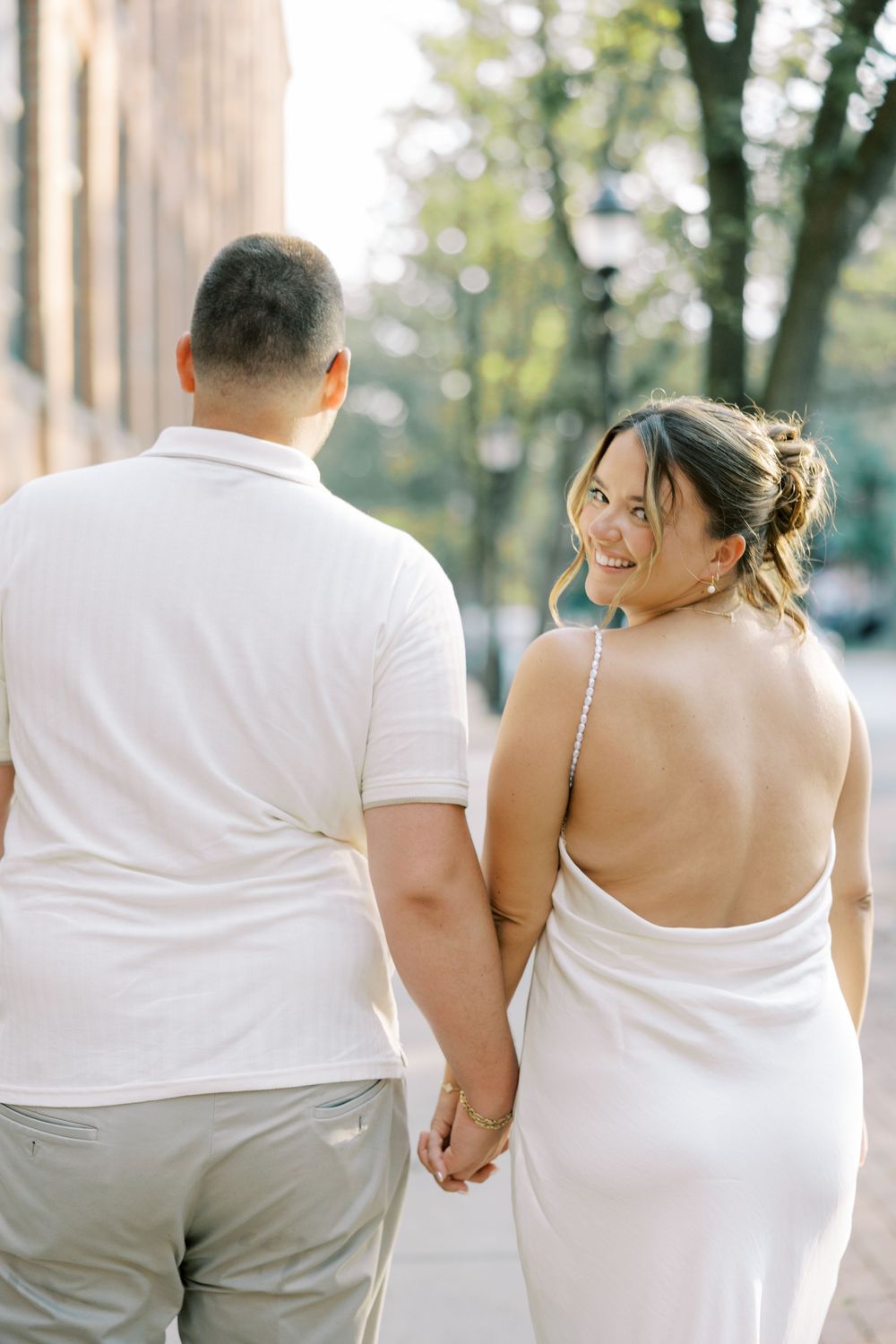 A couple in matching white wedding attire walks together down a walkway, shot from behind in three similar poses.