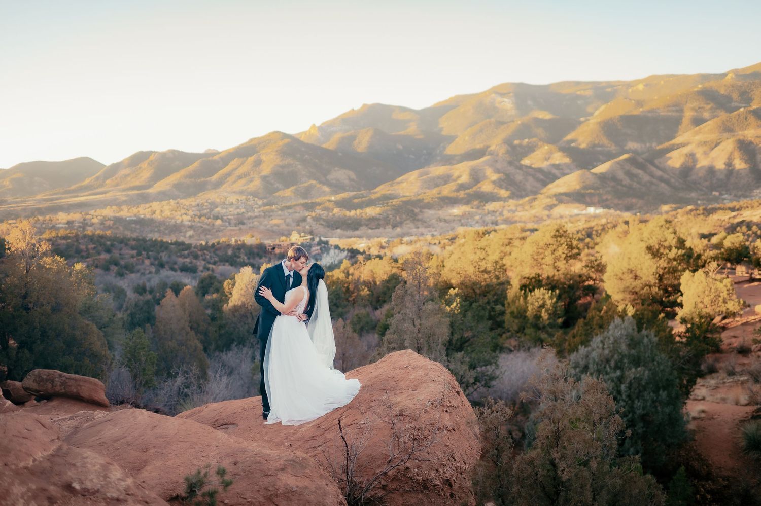 A couple in formal attire stands atop red rock formations in Garden of the Gods during their wedding photoshoot.