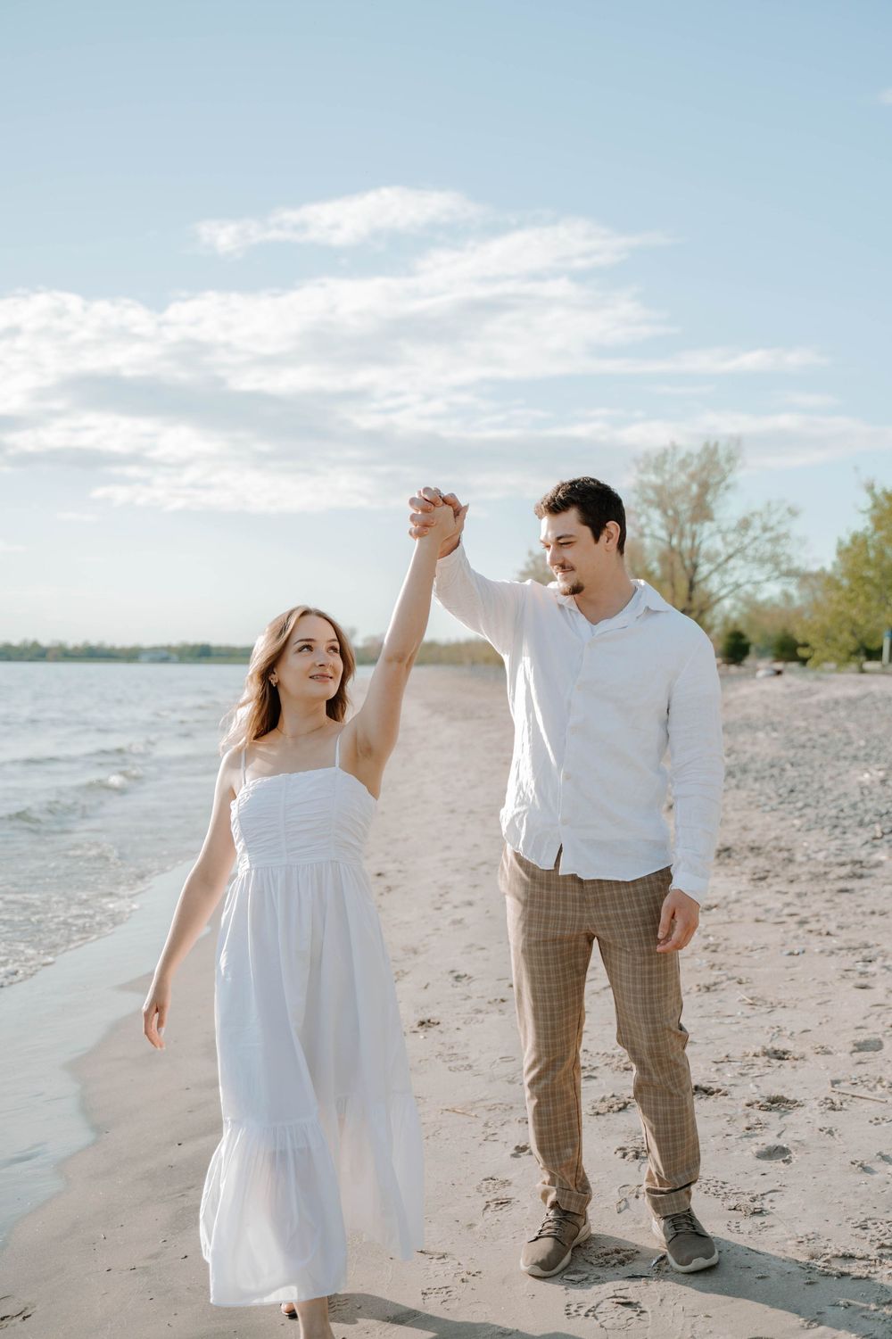 A romantic couple dances and embraces along a serene beach shoreline during a dreamy photo session at sunset.
