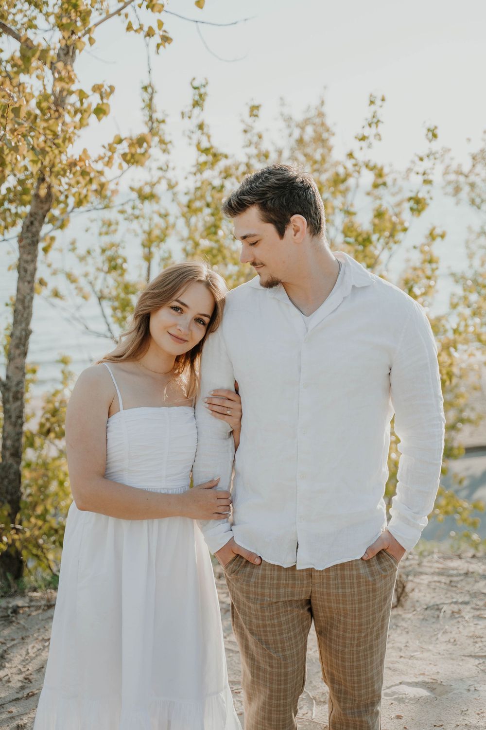 A romantic outdoor couple portrait against autumn trees with soft lighting and elegant white and tan outfits.