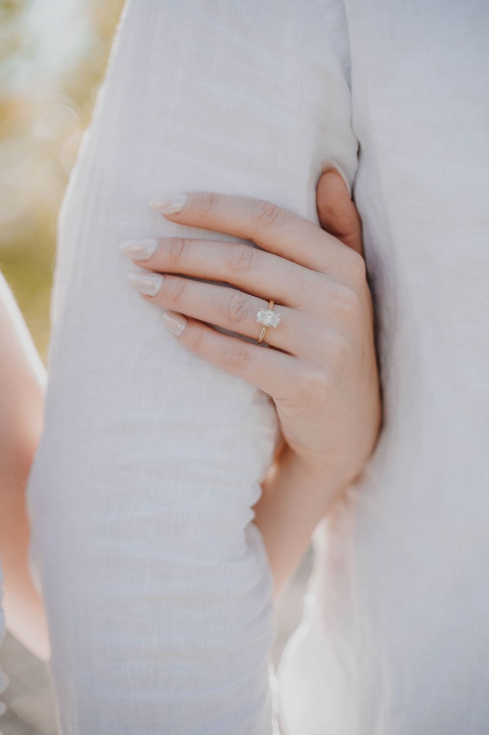 Close-up shot of an engagement ring on a delicate hand against a white fabric background.
