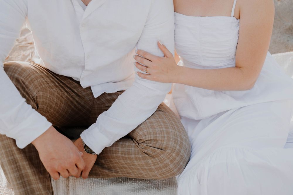 A couple wearing white sitting together in casual romantic pose on light textile background.