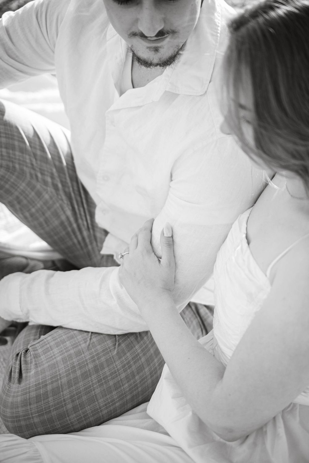 A tender black and white photo showing two people in white outfits holding hands in gentle embrace.