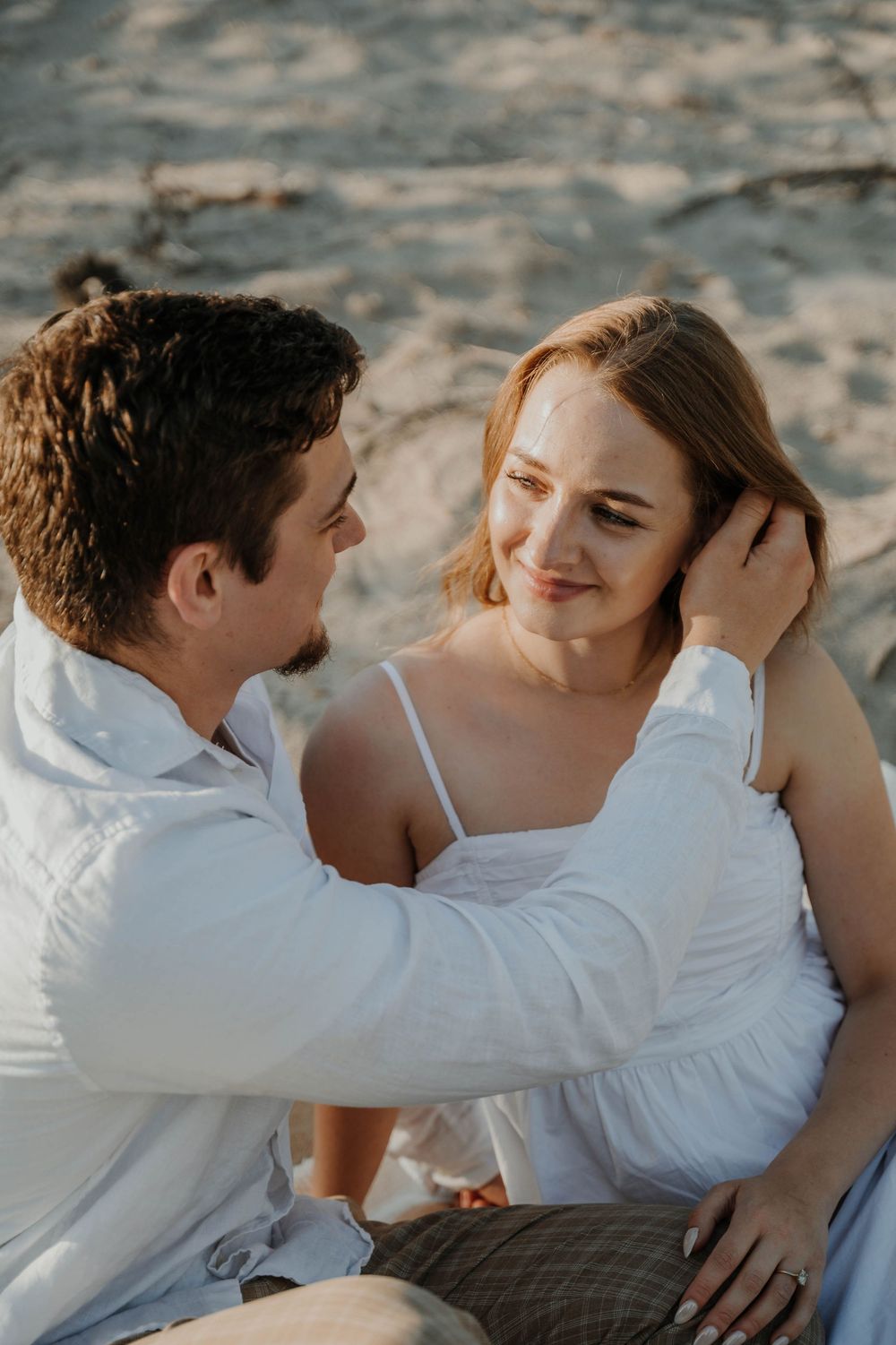 A romantic couple shares an intimate moment outdoors, with the person in white gently touching their partner's hair.