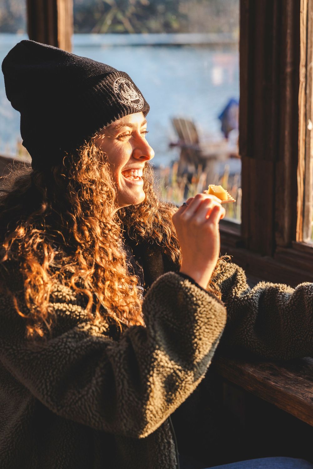 Person in beanie and fuzzy jacket gazes out window during golden hour.