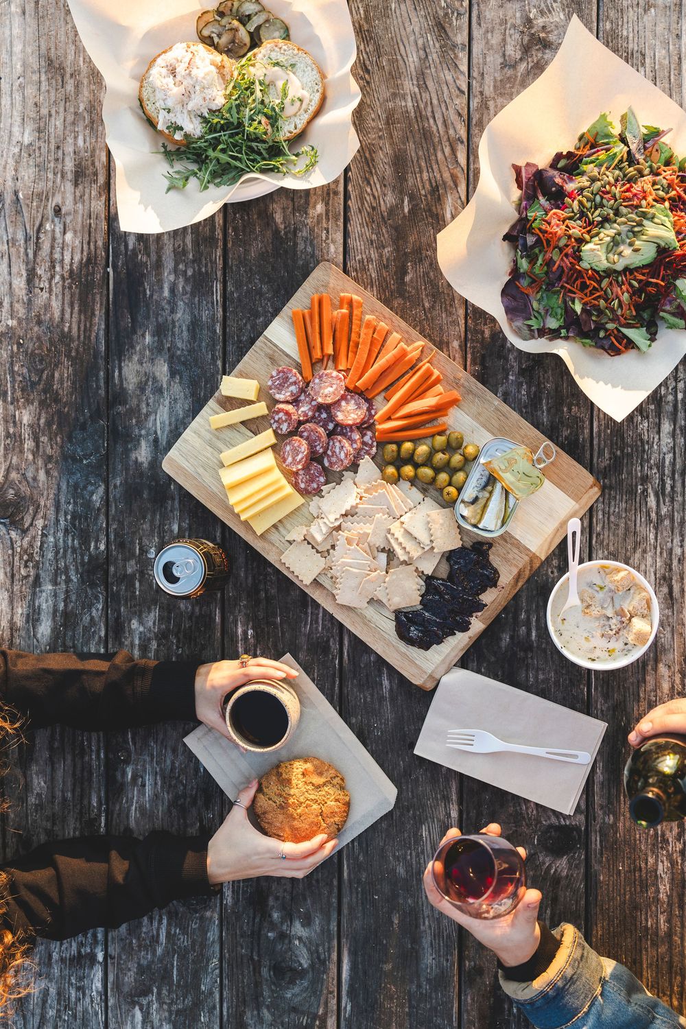 Overhead view of a rustic charcuterie board with meats, cheeses, vegetables and snacks on weathered wood.